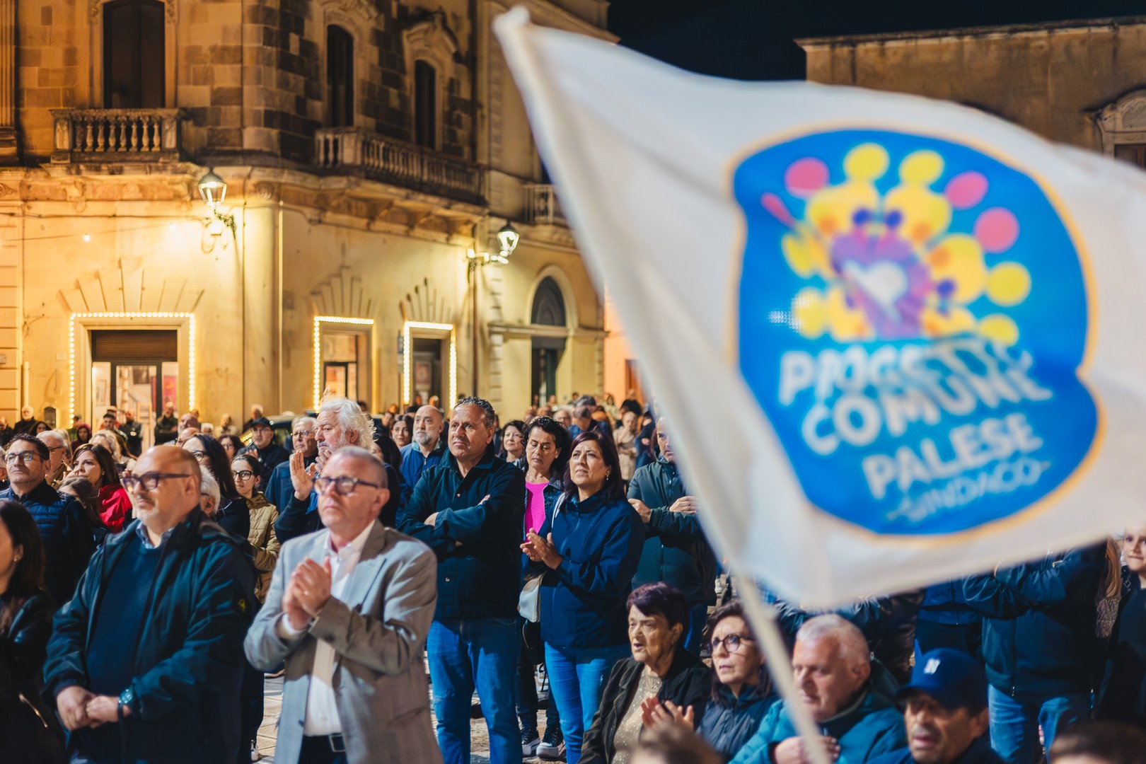 Gruppo di persone che assiste al comizio con cartelli e bandiere